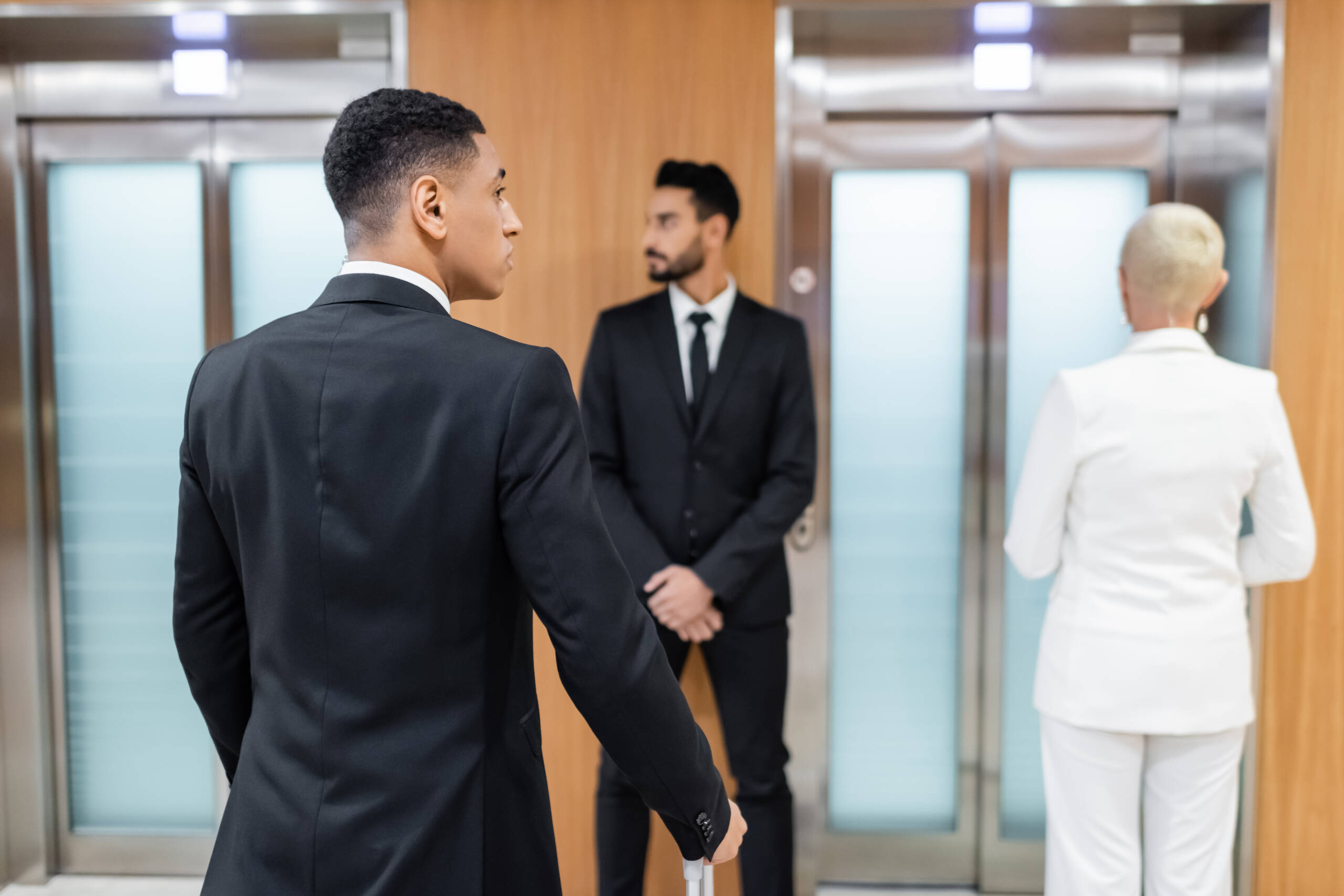 business lady waiting for elevator in hotel near private interracial bodyguards,stock image